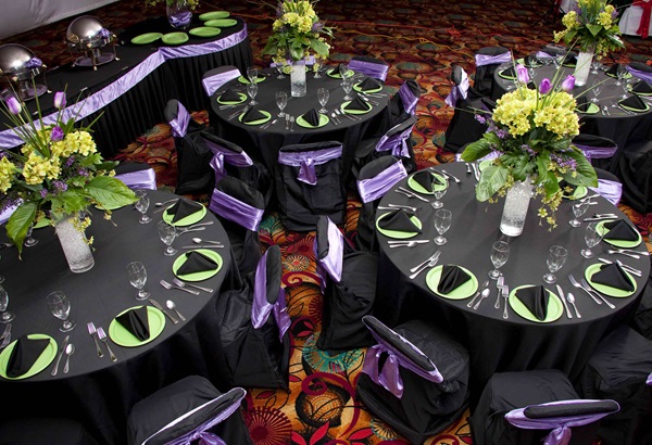 Black, purple and green place settings on banquet table with flower arrangement