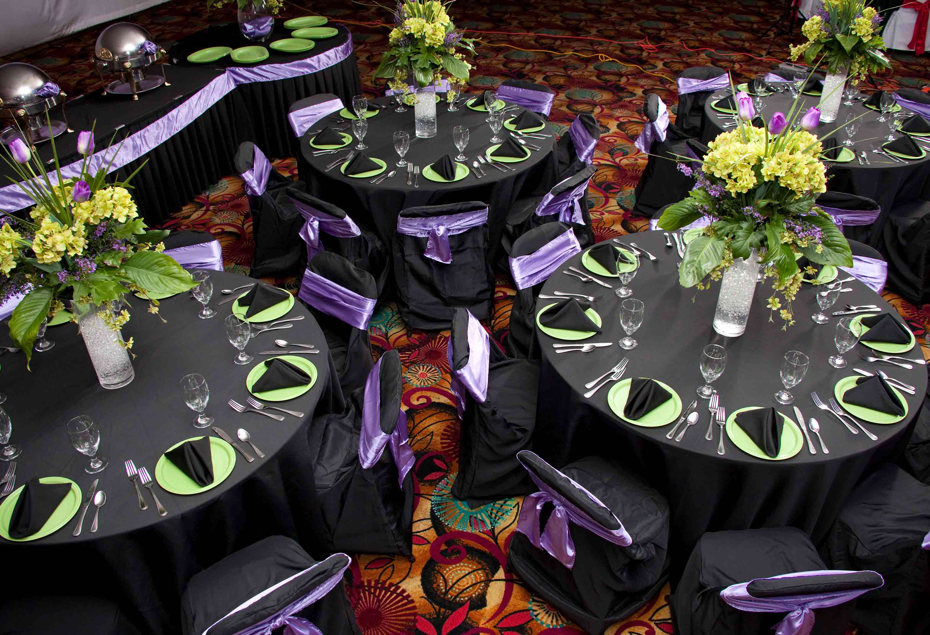Black, purple and green place settings on banquet table with flower arrangement
