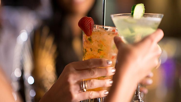 Closeup of Feminine Hands Holding Cocktails at Center Bar